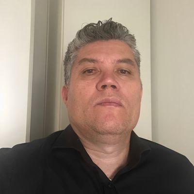 Homem confiante com cabelo grisalho, expressão séria, vestindo camisa preta, retrato close-up.